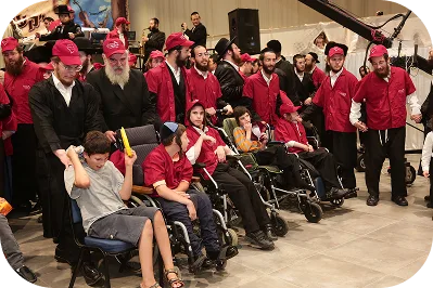 מתנדבי ארגון יד אחת בחולצות אדומות יחד עם ילדים עם מוגבלויות בכיסאות גלגלים באירוע חסד